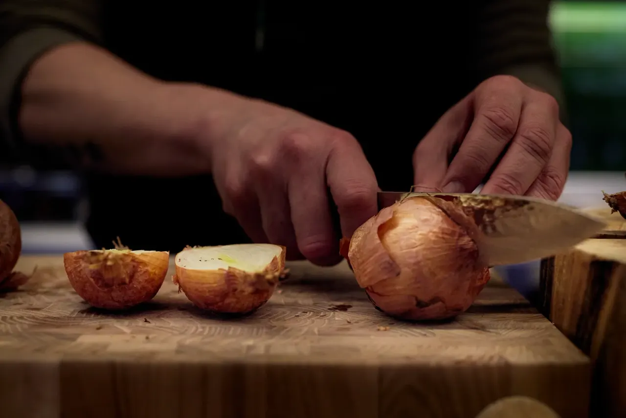 The team's hands cutting roasted onion on the work board of the kitchen at El Invernadero