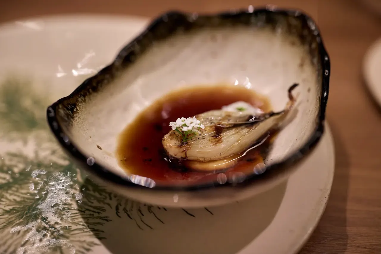 Roasted lettuce heart in its broth, with white flowers, served in a dark-rimmed bowl