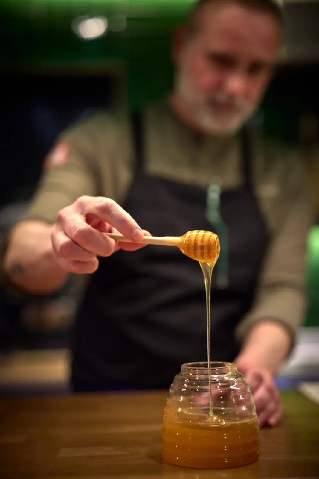 A thread of honey falling from the ladle into a glass, at the counter