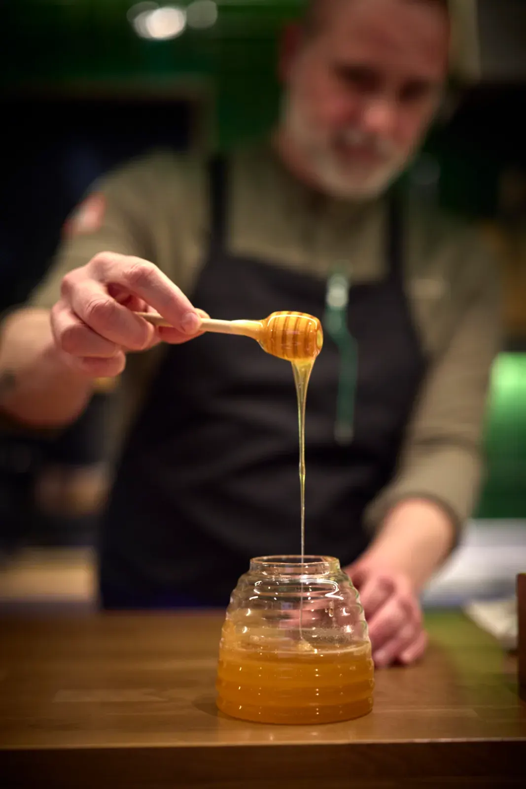A thread of honey falling from the ladle onto the siphon glass, at the counter of El Invernadero