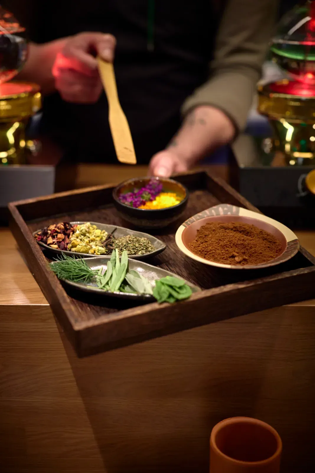 A wooden tray with dried petals, chopped herbs, fresh leaves and a spiced powder, ready for the pass