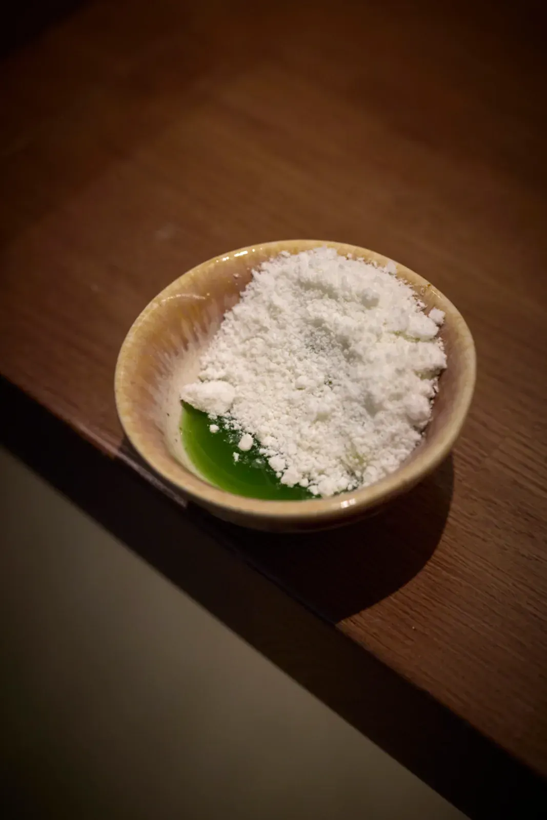 A bowl with a white powder and a fresh green leaf, prepared at the pass