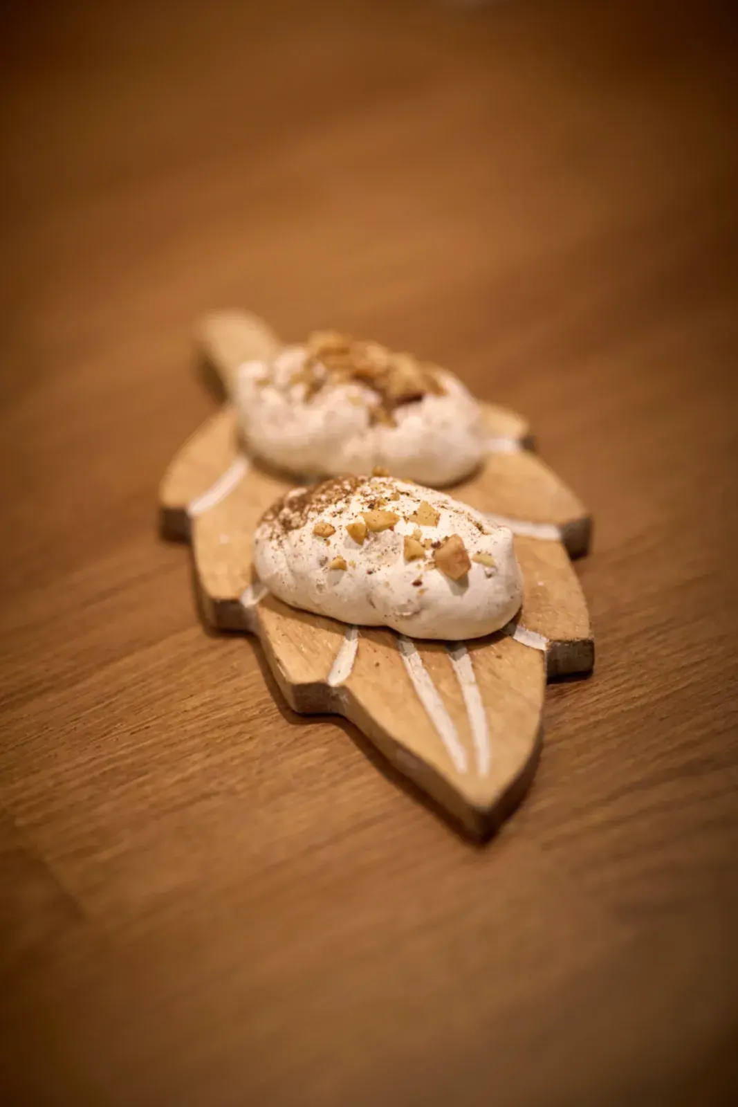 Two white bites topped with golden pieces, on a leaf-shaped wooden board