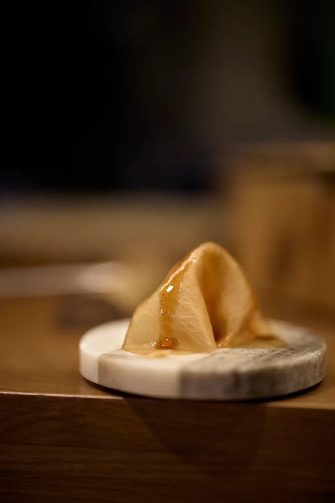 A crisp amber sheet folded on a marble disc, with a thread of golden sauce