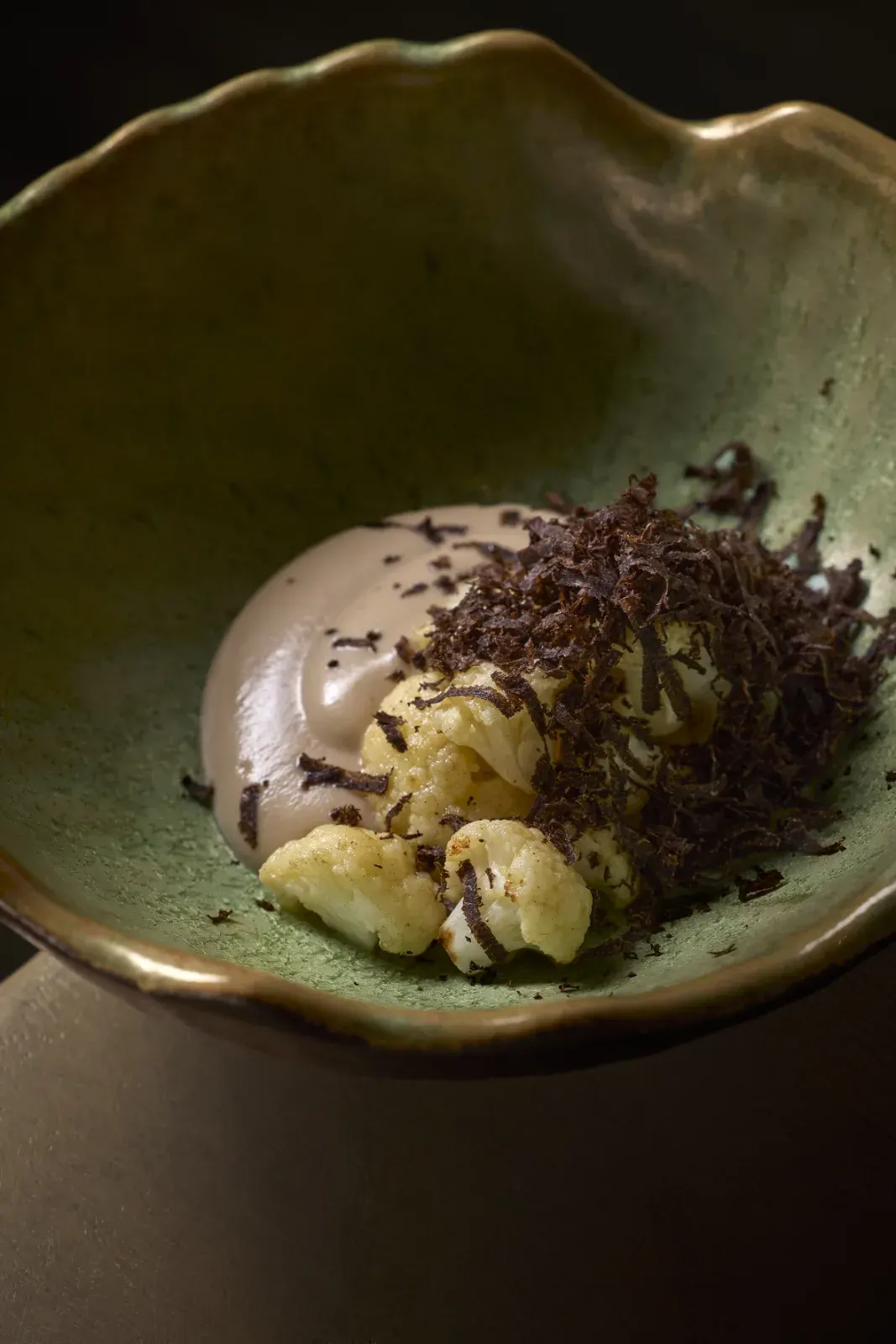 Cauliflower with grated coffee on top, on a green ceramic plate