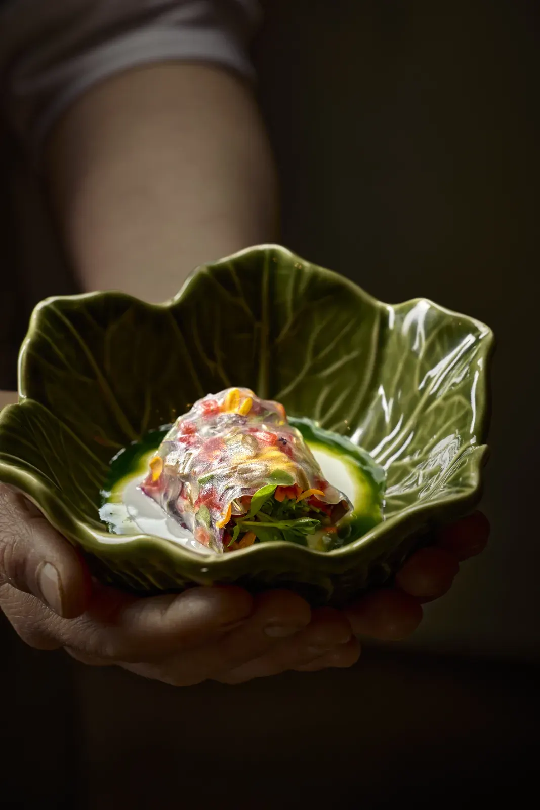 Hands presenting a course served on a leaf-shaped plate