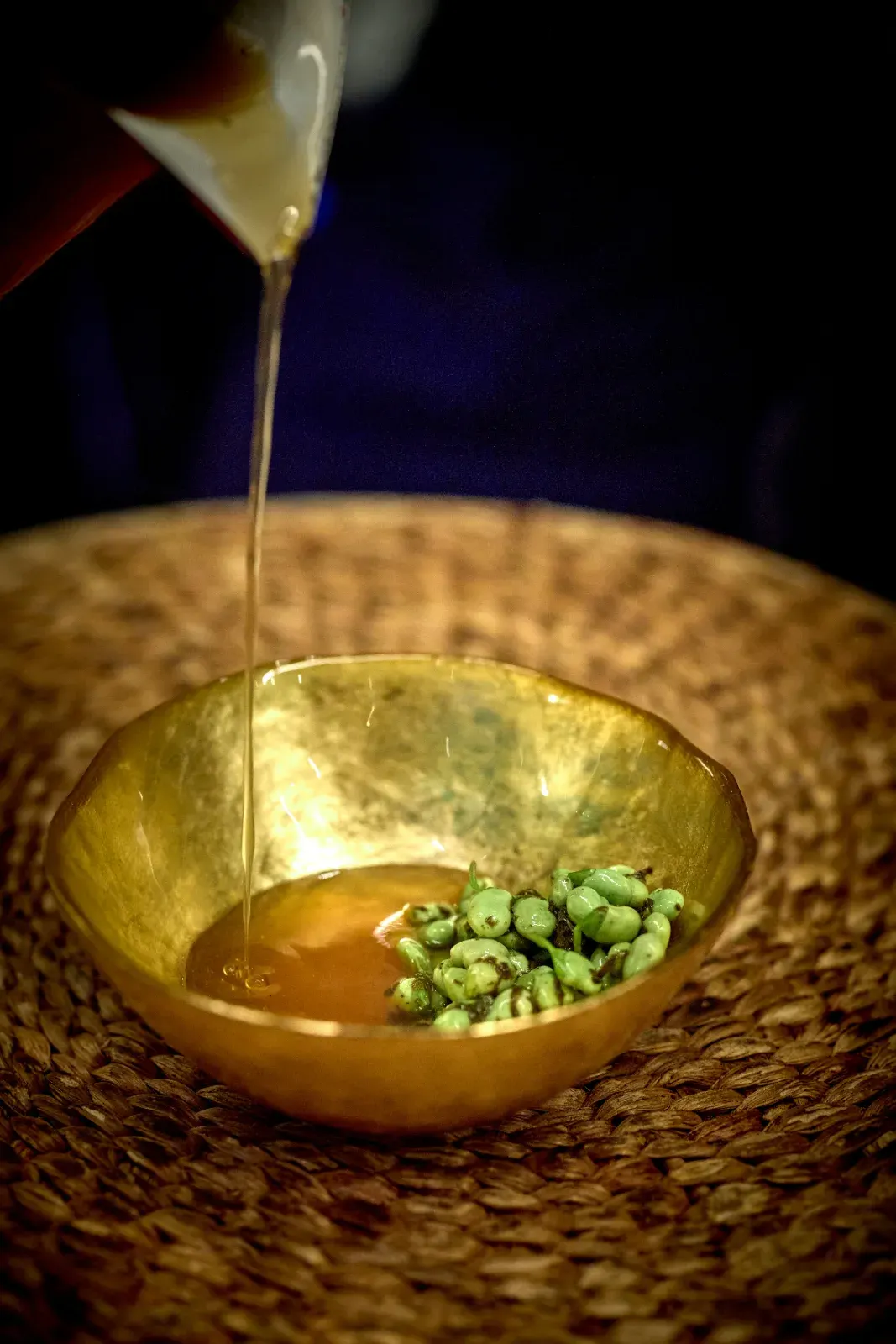 A thread of broth falling over tender green grains, in a golden bowl