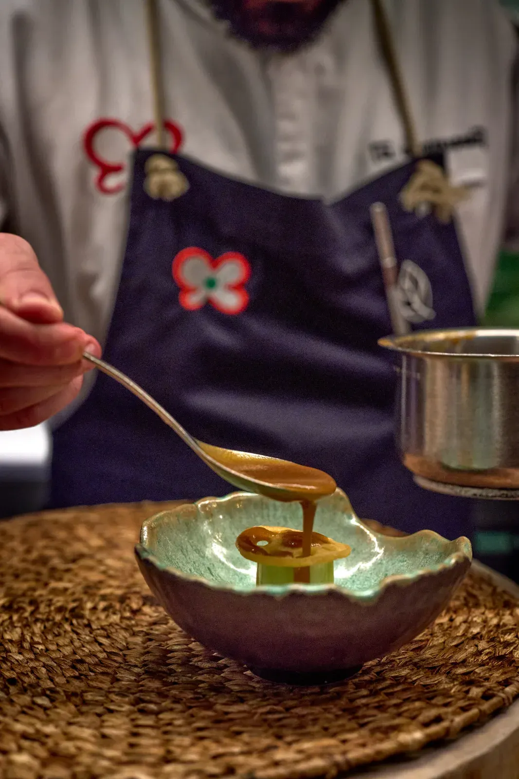A thread of amber sauce falls from the spoon onto the dish, in a ceramic bowl with a green interior
