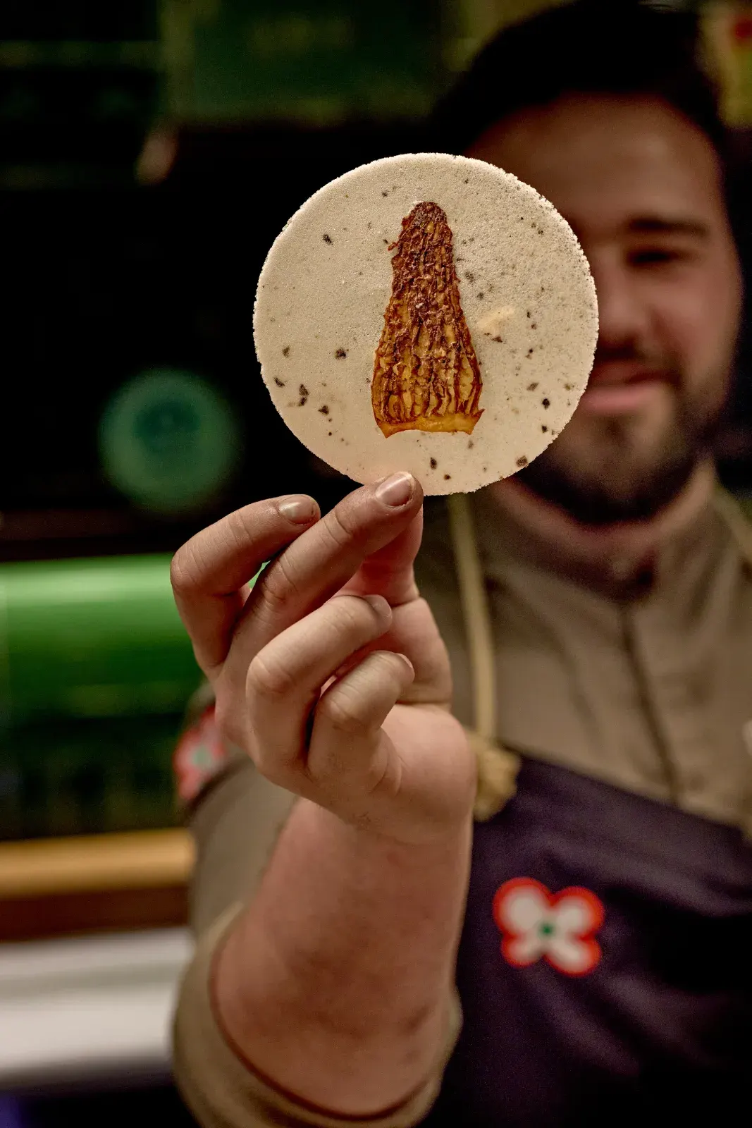 A cook holding a thin wafer with a morel printed in the centre