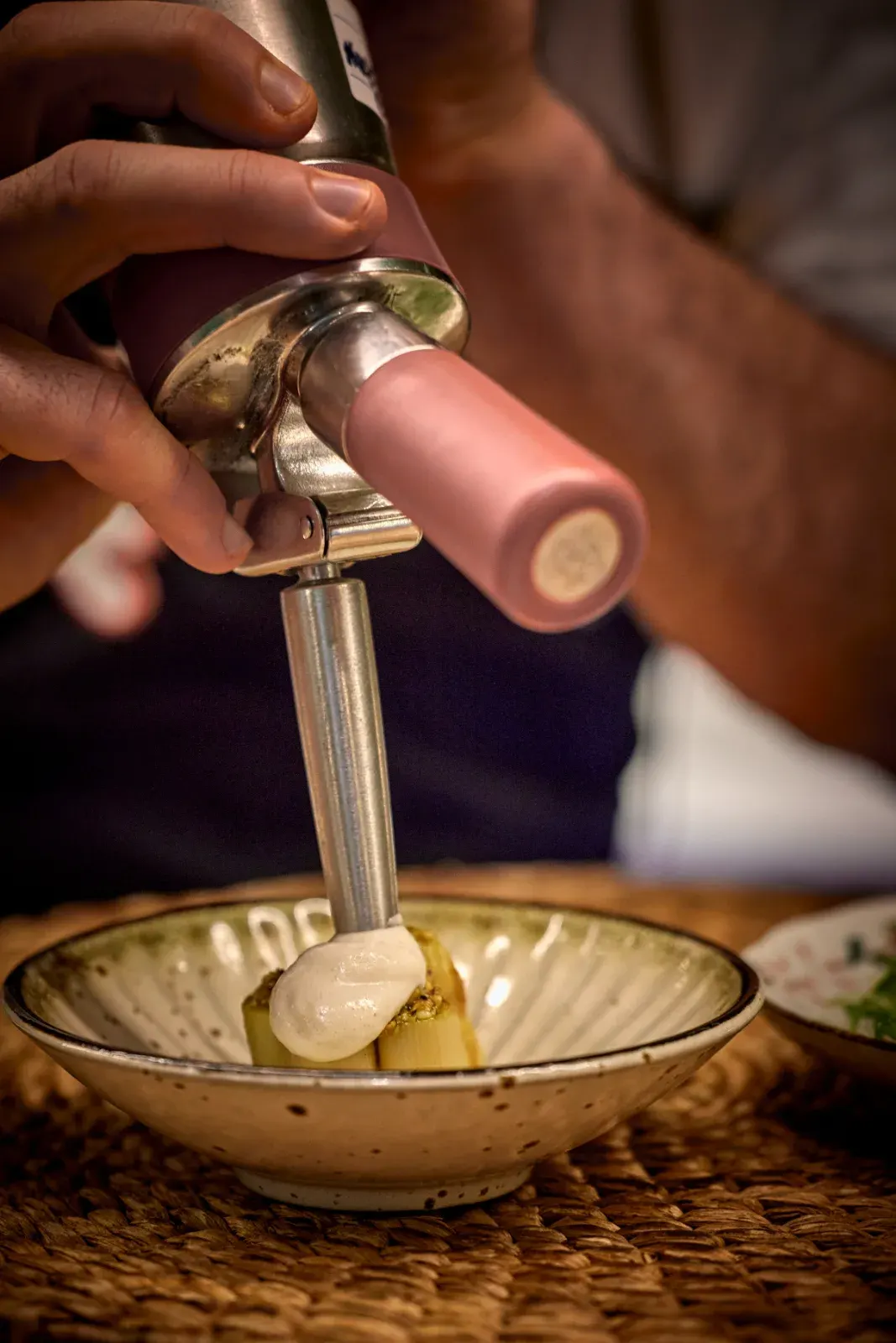 A cook crowning the dish with siphon foam, in a ceramic bowl