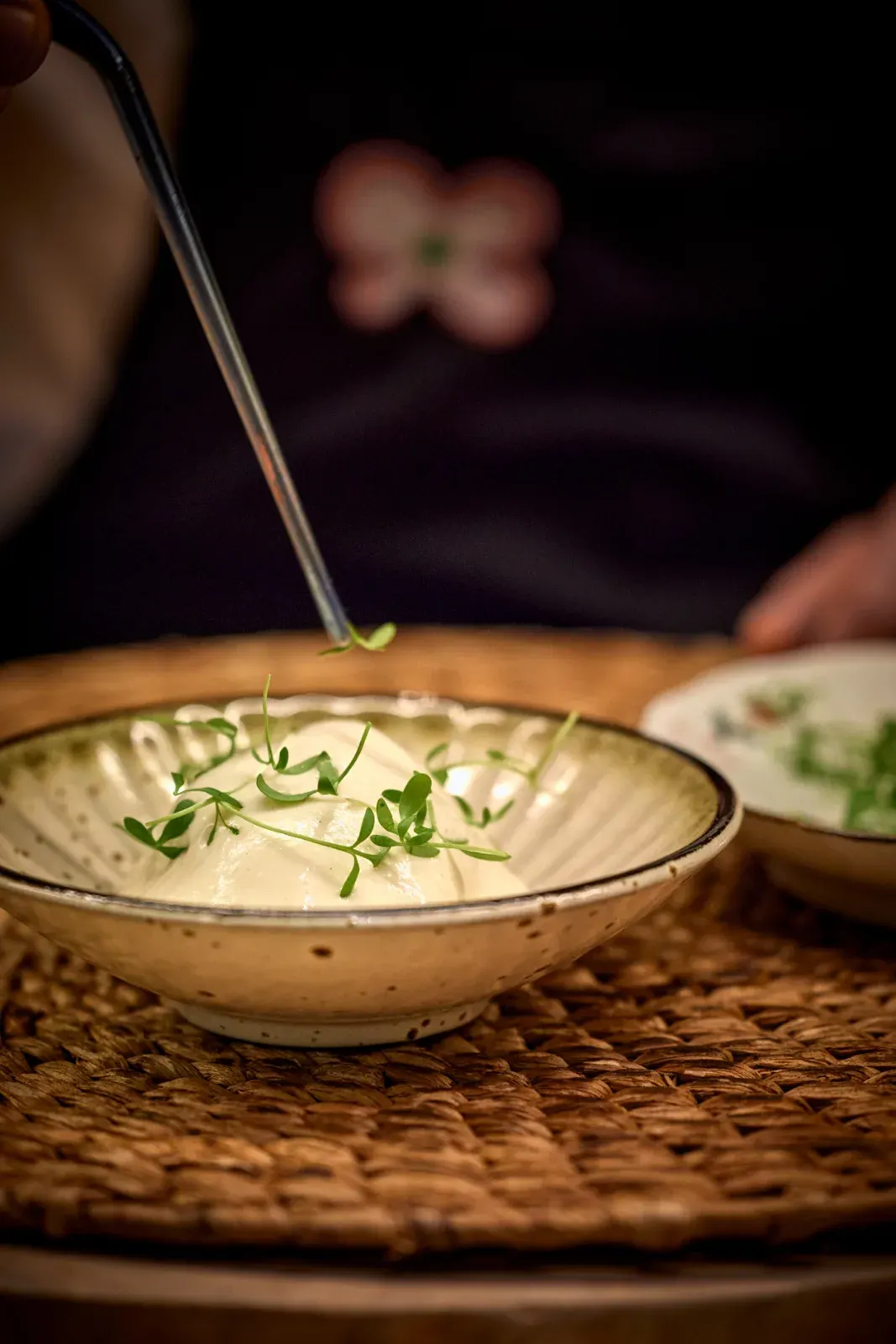 Tweezers finishing a pale cream with green sprouts, served in a ceramic bowl