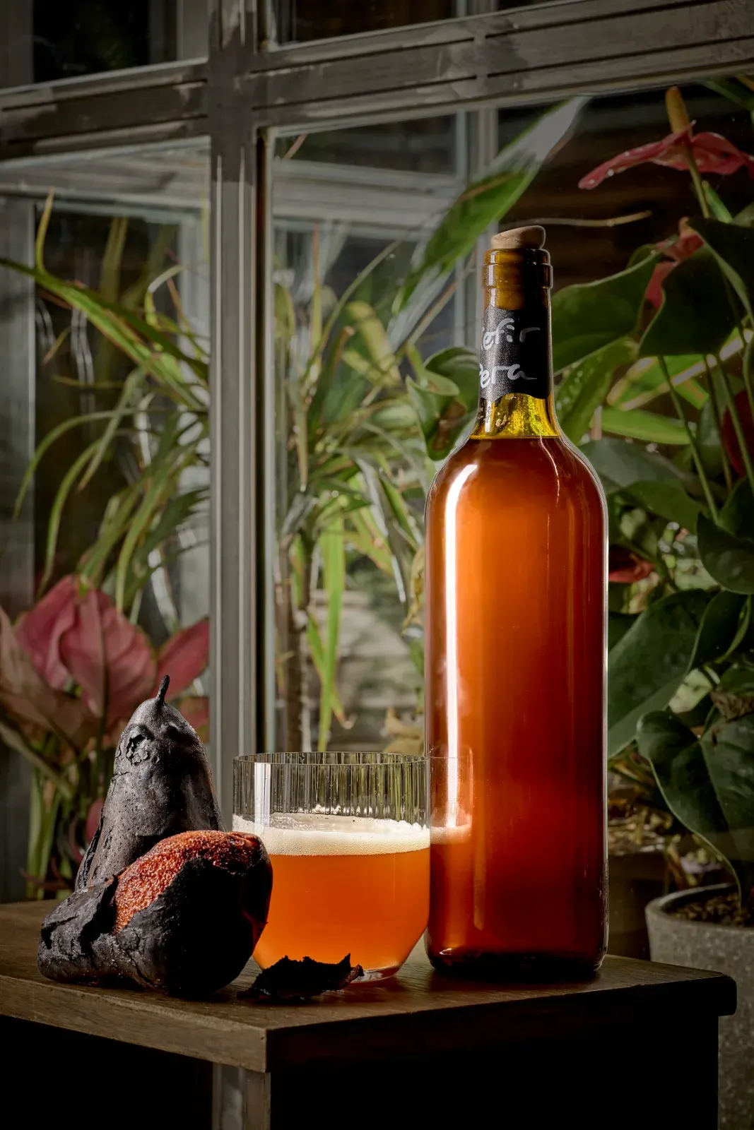 A bottle and glass of pear kefir bottled in house, among the plants of the dining room